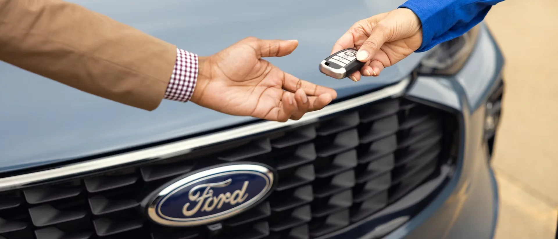 Ford vehicle key fob being handed over in front of a Ford grille — fleet delivery at Envision Ford